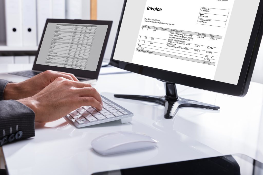 Close-up Of A Businessperson's Hand Checking Invoice On Computer At Workplace